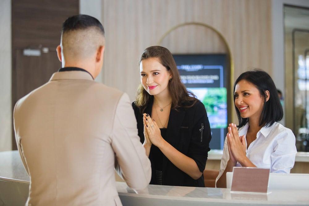 A female business traveler greets the hotel receptionist with a Thai-style greeting