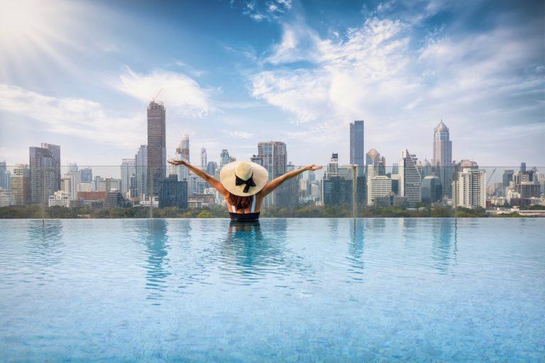 A woman in a pool overlooking the Bangkok skyline after reading a hotel pool guide.